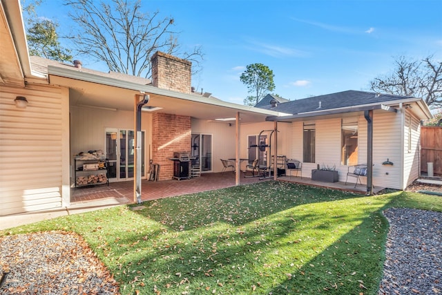 back of house featuring brick siding, a patio area, a lawn, and a chimney