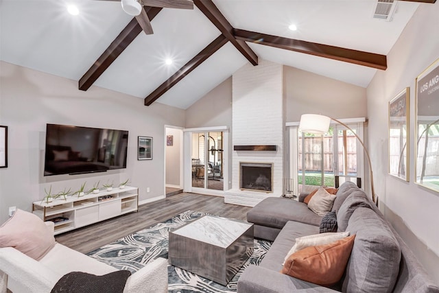 living area featuring visible vents, beam ceiling, a brick fireplace, and wood finished floors