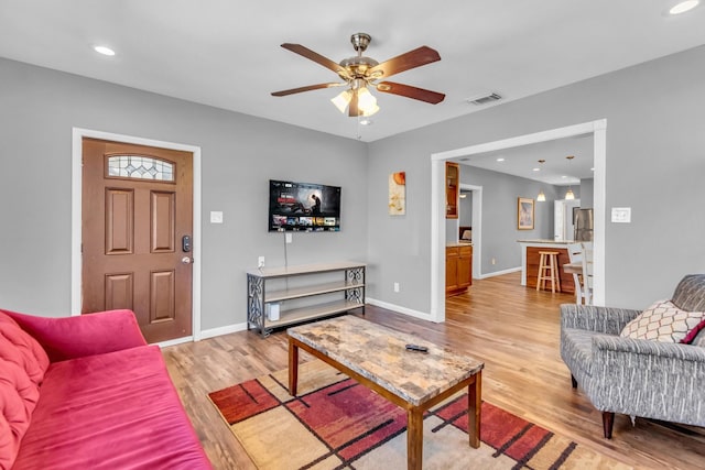 living room with light wood-type flooring, baseboards, visible vents, and ceiling fan