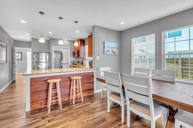 kitchen featuring light stone counters, light wood-type flooring, a peninsula, appliances with stainless steel finishes, and brown cabinets