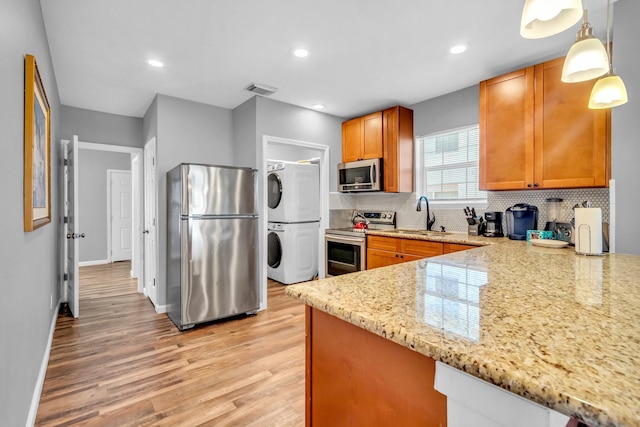 kitchen with light wood-style flooring, a sink, tasteful backsplash, stacked washing maching and dryer, and appliances with stainless steel finishes