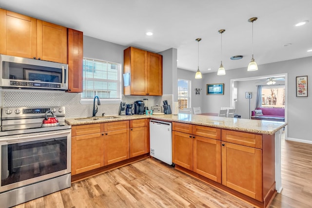 kitchen with light wood finished floors, a peninsula, a sink, appliances with stainless steel finishes, and backsplash