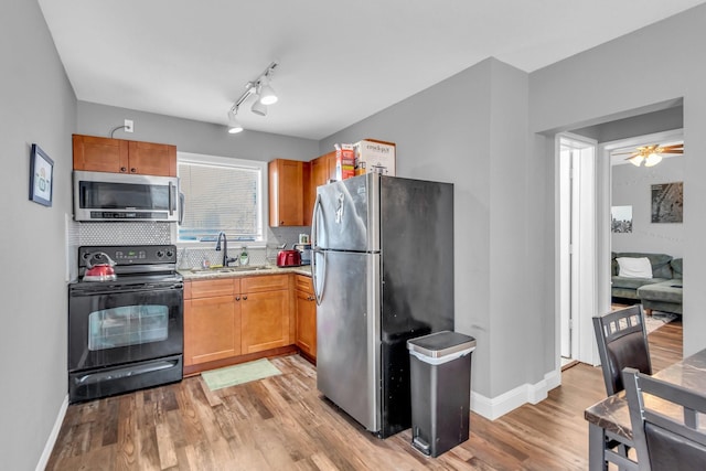 kitchen with tasteful backsplash, baseboards, light wood-style flooring, stainless steel appliances, and a sink