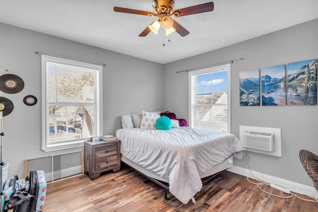 bedroom with an AC wall unit, wood finished floors, and baseboards