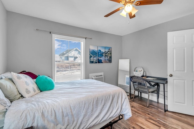 bedroom featuring a ceiling fan, a wall unit AC, and wood finished floors