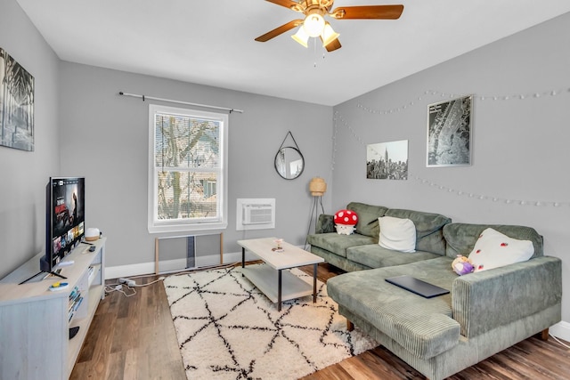 living room with an AC wall unit, wood finished floors, baseboards, and ceiling fan