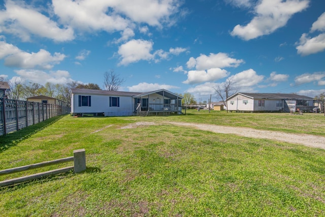 rear view of house with fence, a yard, and dirt driveway