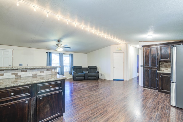 kitchen featuring decorative backsplash, dark brown cabinetry, dark wood-style flooring, and freestanding refrigerator