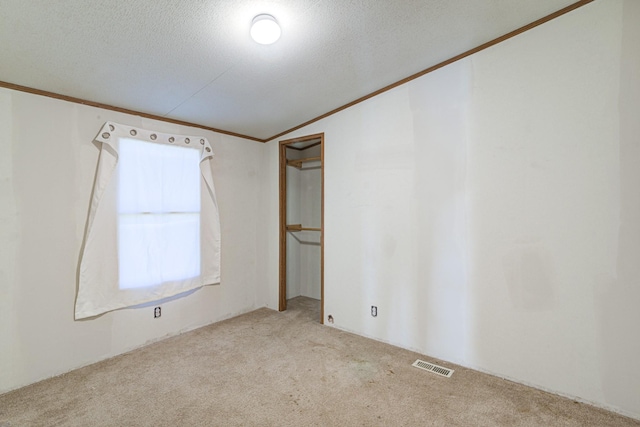 empty room featuring visible vents, a textured ceiling, crown molding, and carpet