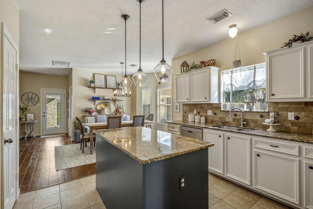 kitchen with tasteful backsplash, a kitchen island, dishwasher, white cabinets, and a sink