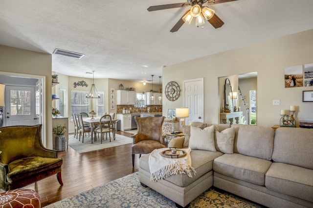 living room with visible vents, a textured ceiling, dark wood-type flooring, and a ceiling fan