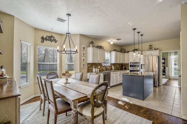 dining space featuring a notable chandelier, a textured ceiling, light wood-type flooring, and visible vents