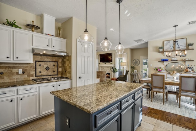 kitchen featuring light tile patterned floors, stone counters, stainless steel gas stovetop, under cabinet range hood, and white cabinetry