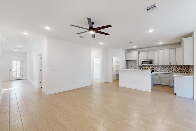 kitchen with light wood-type flooring, visible vents, stainless steel microwave, backsplash, and open floor plan