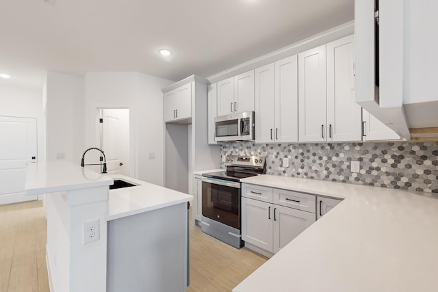 kitchen with backsplash, light countertops, light wood-style flooring, stainless steel appliances, and a sink