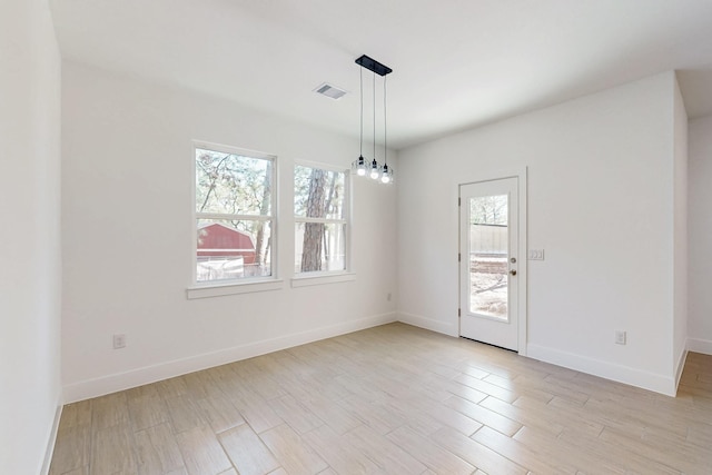 empty room featuring an inviting chandelier, light wood-style flooring, baseboards, and visible vents