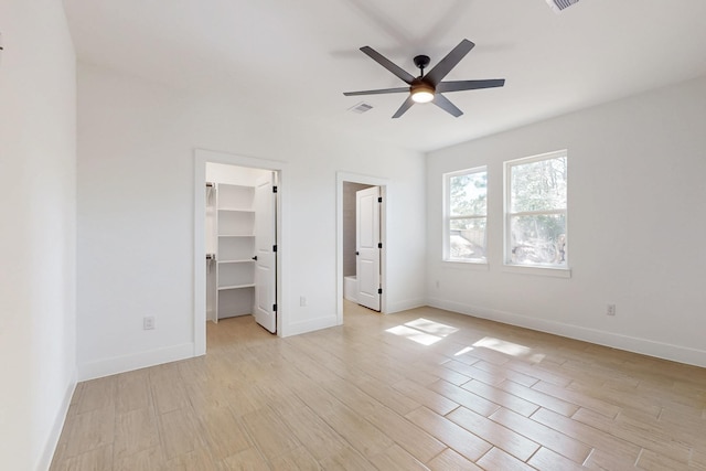 unfurnished bedroom with a spacious closet, visible vents, light wood-type flooring, and baseboards