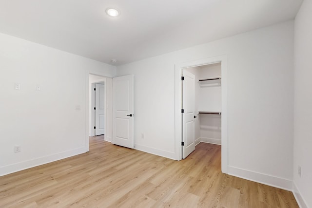 unfurnished bedroom featuring a walk in closet, baseboards, and light wood finished floors