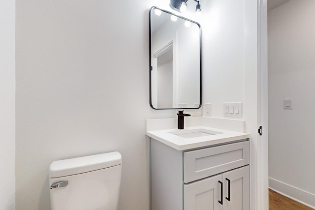 half bathroom with baseboards, toilet, wood finished floors, and vanity