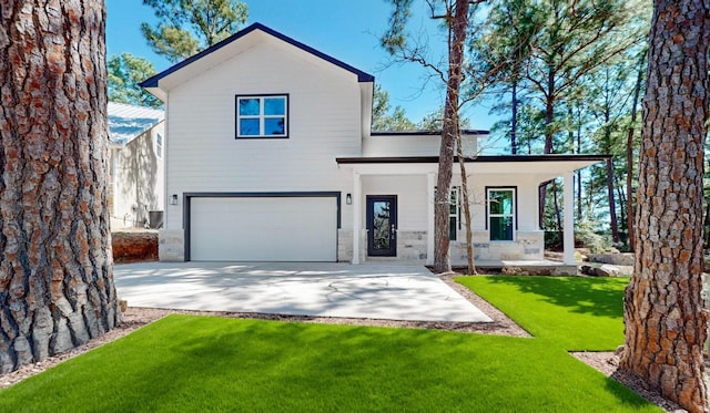 view of front of property with driveway, stone siding, covered porch, an attached garage, and a front yard