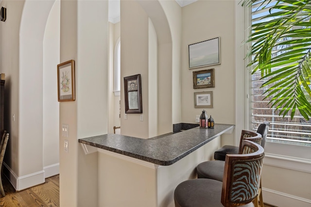 bar with arched walkways, baseboards, and wood finished floors