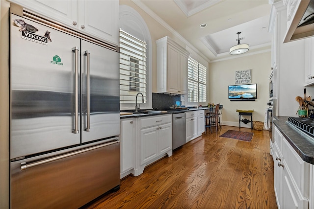 kitchen featuring a sink, dark countertops, white cabinets, crown molding, and built in appliances