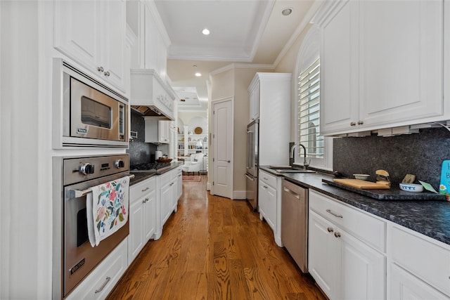 kitchen with wood finished floors, a sink, stainless steel appliances, white cabinetry, and crown molding