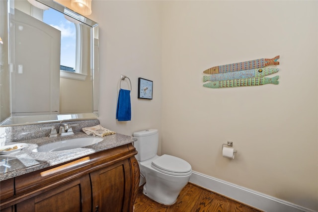 half bath with vanity, toilet, wood finished floors, and baseboards