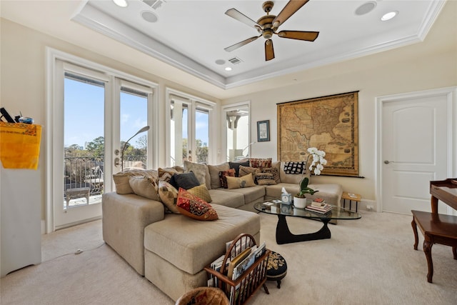 living area featuring a tray ceiling, a ceiling fan, visible vents, and light carpet