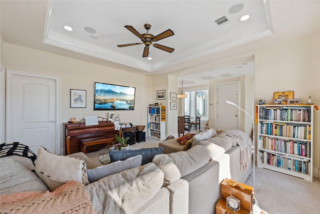 living area with a tray ceiling, carpet flooring, a ceiling fan, and visible vents