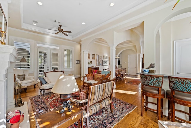 living area featuring wood finished floors, visible vents, a tray ceiling, decorative columns, and arched walkways