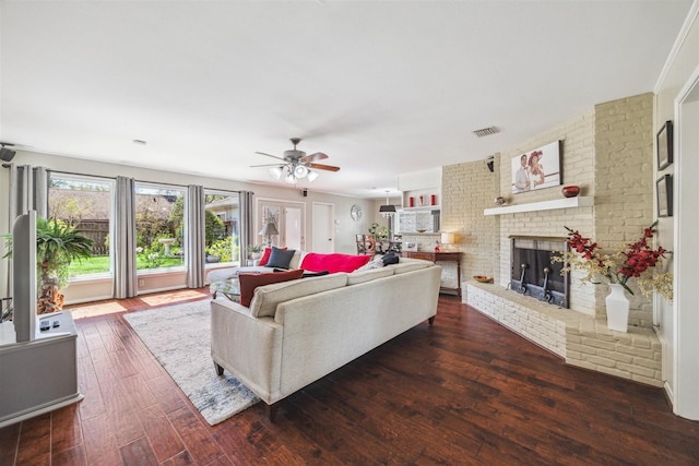 living area featuring visible vents, dark wood-type flooring, a brick fireplace, and ceiling fan