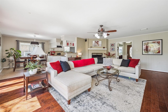 living area with visible vents, ornamental molding, a ceiling fan, wood-type flooring, and a fireplace