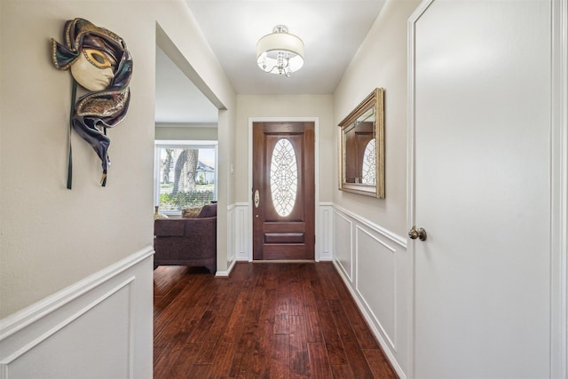 entryway with dark wood finished floors, a decorative wall, wainscoting, and an inviting chandelier