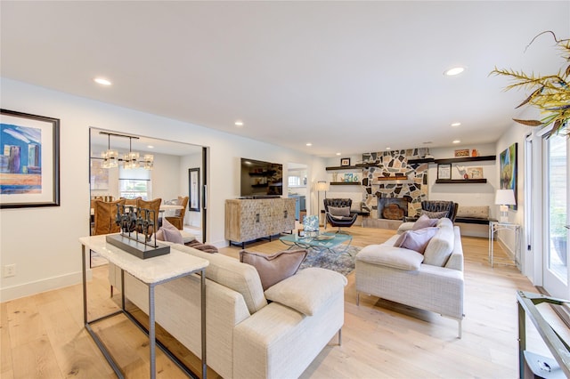 living area with recessed lighting, light wood-type flooring, a notable chandelier, and a stone fireplace