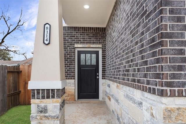 view of exterior entry with brick siding and fence