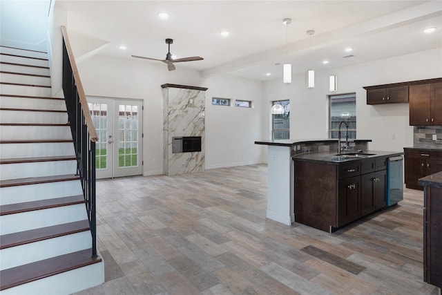 kitchen with dark countertops, dark brown cabinetry, open floor plan, light wood-style flooring, and a sink