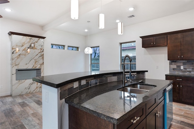 kitchen featuring visible vents, an island with sink, a sink, backsplash, and light wood finished floors