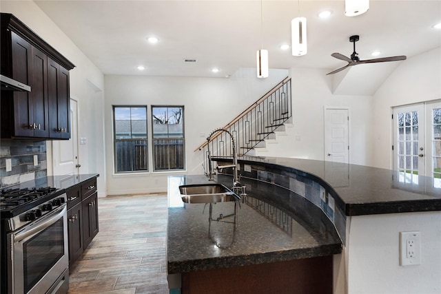 kitchen with stainless steel gas range oven, light wood finished floors, dark stone counters, an island with sink, and a sink