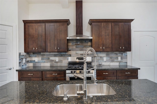 kitchen with a sink, dark brown cabinets, stainless steel gas range oven, wall chimney exhaust hood, and tasteful backsplash