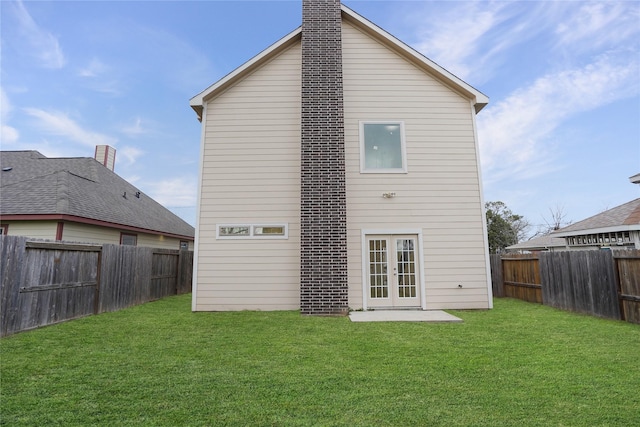 rear view of house with a fenced backyard, french doors, a chimney, and a yard