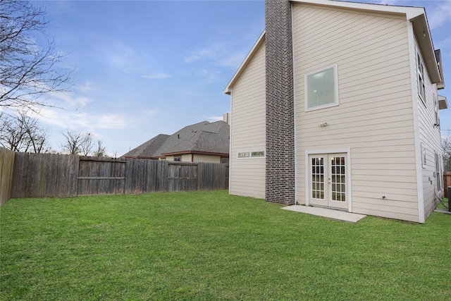 back of house featuring a yard, a fenced backyard, a chimney, and french doors