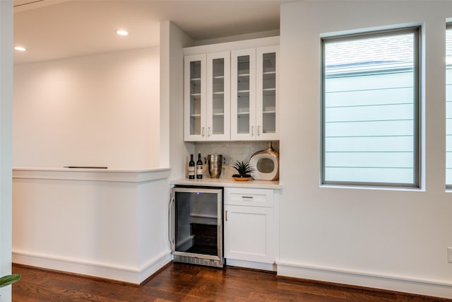 bar featuring dark wood-type flooring, wine cooler, a baseboard heating unit, a dry bar, and backsplash