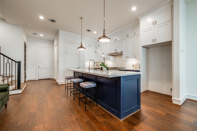 kitchen featuring dark wood-style floors, light countertops, white cabinets, under cabinet range hood, and backsplash