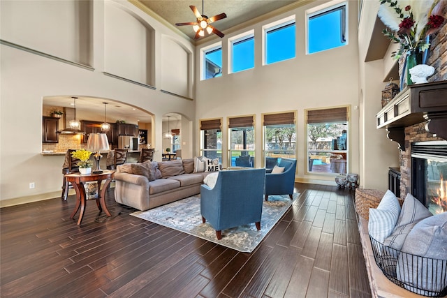 living room with ceiling fan, baseboards, wood finish floors, a stone fireplace, and arched walkways