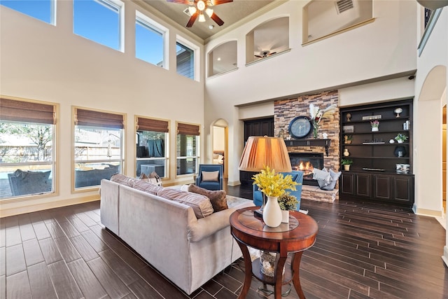 living area with baseboards, visible vents, wood tiled floor, a stone fireplace, and crown molding