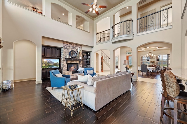 living area with stairway, baseboards, a fireplace, dark wood-type flooring, and ceiling fan with notable chandelier