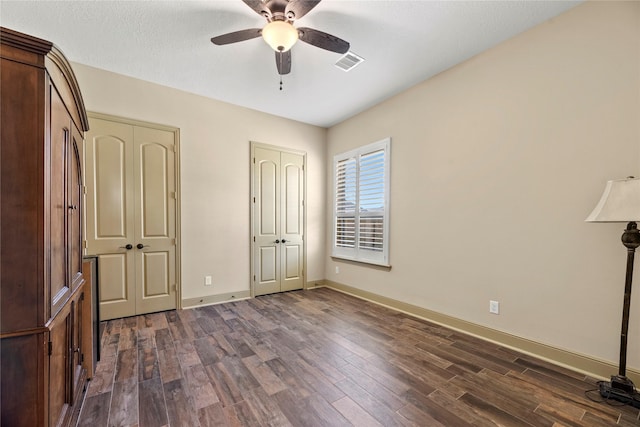 unfurnished bedroom with ceiling fan, visible vents, baseboards, and dark wood finished floors