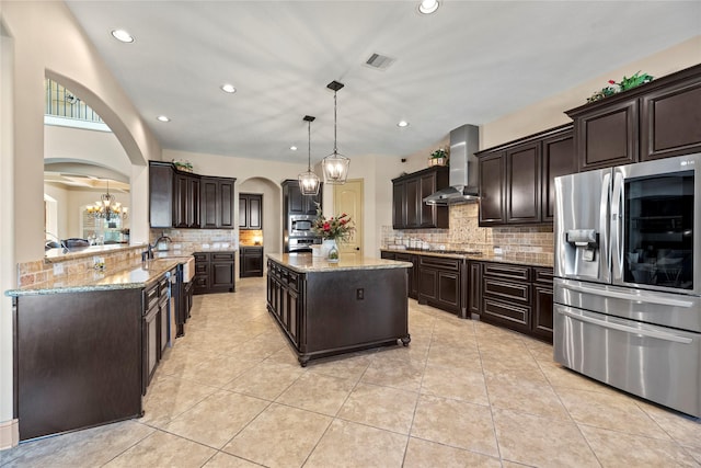 kitchen featuring visible vents, dark brown cabinets, wall chimney range hood, arched walkways, and stainless steel appliances