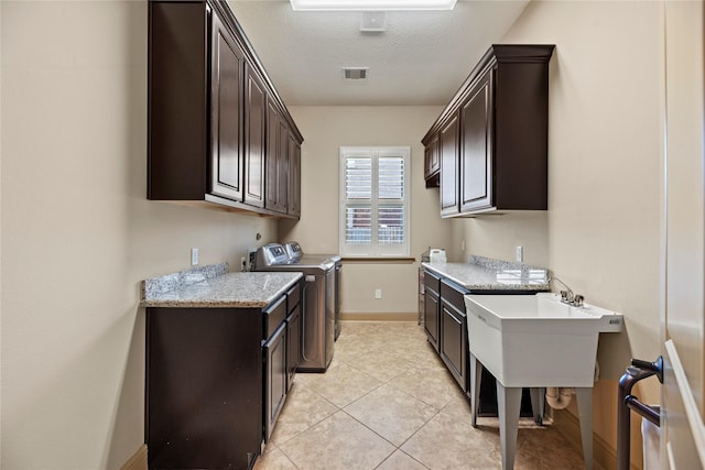 kitchen with light tile patterned floors, baseboards, dark brown cabinets, a textured ceiling, and washer and dryer